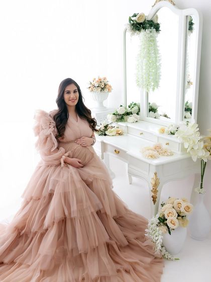 A portrait of pure elegance. This mom-to-be looks absolutely stunning in a ruffled, floor-length beige gown, surrounded by soft white florals in our studio.