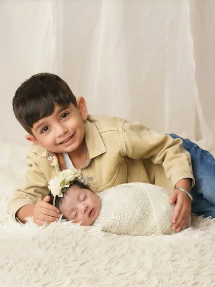 A big brother lies next to his sleeping newborn sister, a protective and sweet gesture. This showcases the gentle beginning of their sibling relationship.