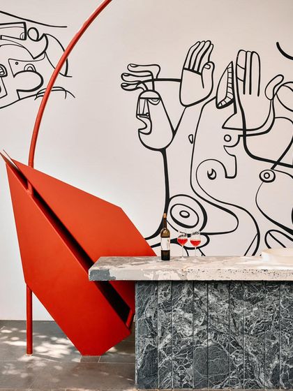 A detail of the outdoor bar area, where a sculpted red metal form contrasts with the green marble and a hand-painted wall mural.