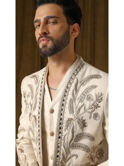 A close-up of the 'Pragyan' shrug set, highlighting the intricate cream and gold garden-inspired embroidery on the luxurious ivory fabric.