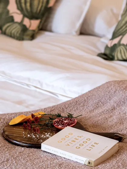 A cozy bedroom scene with a book titled "Good Vibes, Good Life" resting on a wooden tray with fresh fruit. This image perfectly captures a mood of relaxation, positivity, and self-care.