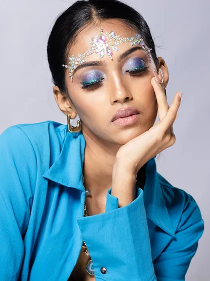A creative beauty portrait featuring a bejeweled headpiece and vibrant blue eyeshadow. The composition is artistic and perfect for a beauty editorial.