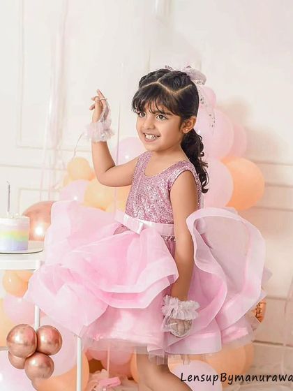 A little princess in a beautiful, fluffy pink dress smiles brightly during her birthday celebration, surrounded by festive pastel balloons and a birthday cake.