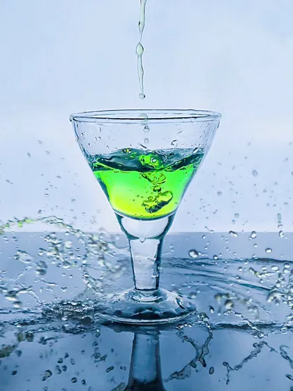 A vibrant green drink being poured into a glass, with surrounding splashes creating a refreshing and energetic scene.
