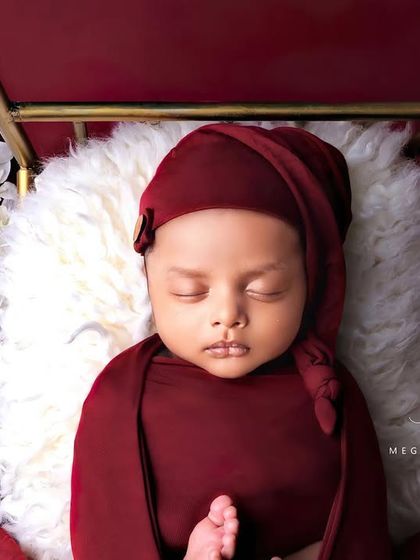A baby in a red sleepy cap, resting on a golden bed with white flowers.
