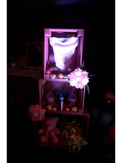 A sweet display of baby items, like a onesie and a milk bottle, arranged in stacked wooden crates and softly lit to create a warm, loving corner.