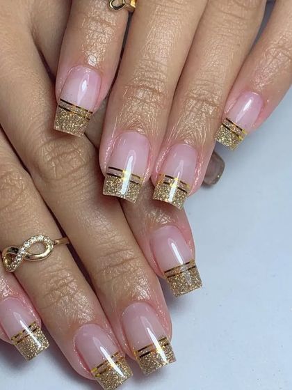 An elegant French manicure with a twist, featuring gold glitter tips with a clean, thin gold line for separation.