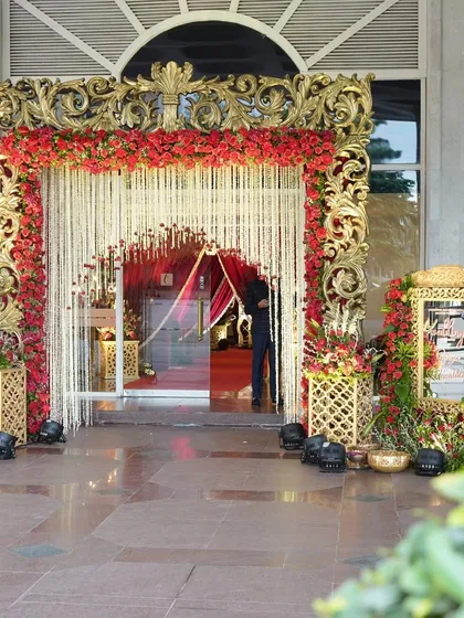 An ornate, gold-carved frame adorned with red roses and a curtain of white tuberoses creates a truly royal entrance for a grand wedding celebration.