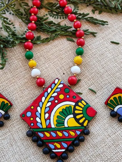 An artistic, diamond-shaped pendant necklace with a flower and leaf design, here in a vibrant red base with multi-color details.