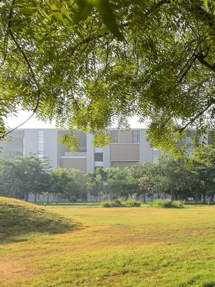 The architecture of Ahmedabad University is set within a carefully sculpted landscape of rolling green lawns and mature trees. The building appears as a quiet, considered backdrop to the natural environment.