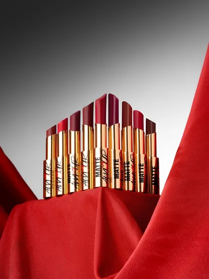 A powerful product shot that arranges these matte lipsticks into a crown-like formation. The dramatic lighting on the rich red fabric creates a sense of luxury and desire, perfect for a beauty brand campaign.