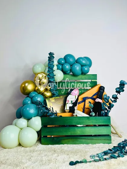 A vibrant green and teal gift crate, artfully arranged with presents and a matching balloon garland.