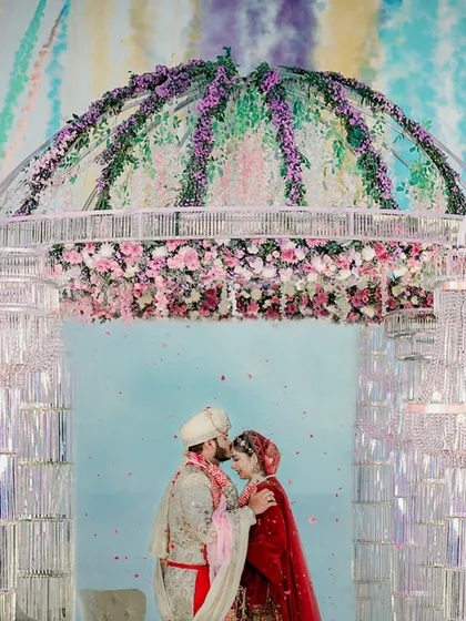 A picture-perfect varmala moment from a Goa beach wedding. The crystal mandap, floral dome, and colorful backdrop all came together to frame the couple's love.
