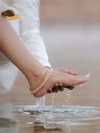 An artistic and symbolic close-up of a groom washing his bride's feet in the water of a temple pond, a beautiful gesture of love and respect.