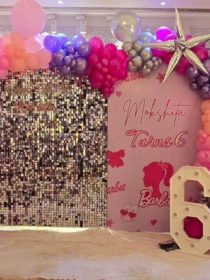 A vibrant Barbie themed birthday setup for a 6th birthday, with a silver sequin wall and pink and purple balloon decor.