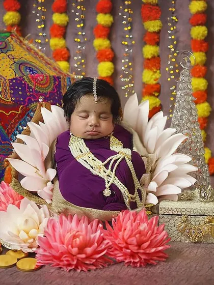 Another beautiful Navratri setup, full of vibrant colors and traditional elements. The baby is surrounded by marigolds, a decorative umbrella, and gold coins, creating a rich and festive scene.