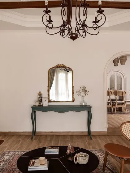 The living area is designed with multiple archways to create an open, flowing feel between rooms. A vintage-style console table in a muted green adds a touch of color, connecting the space back to the exterior accents.