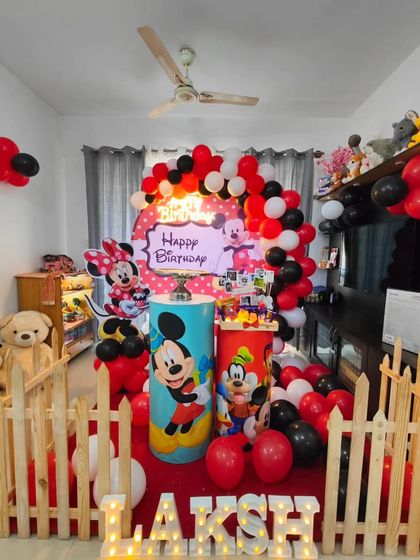 A classic Mickey Mouse Clubhouse theme for a little one's birthday. This home decoration features Mickey, Minnie, and Goofy cutouts, a red, black, and white balloon arch, and a personalized name display.