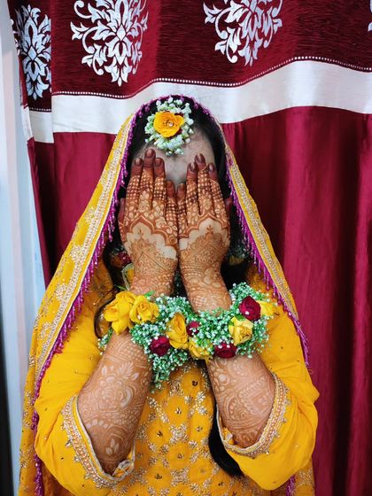 The classic bridal pose, showing off the detailed henna work. The floral gajra and yellow outfit make the fresh mehendi design pop.