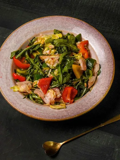 A fresh arugula and chicken salad with colorful bell peppers. The moody lighting and dark plate create a sophisticated image for a cafe or restaurant menu.