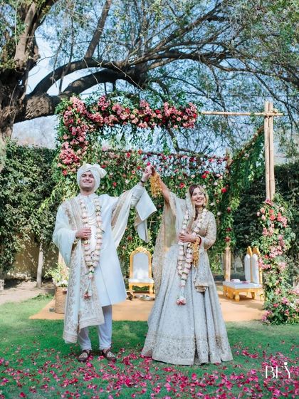 The couple stands together after their varmala exchange, showered in petals, with their beautiful garden mandap in the background.