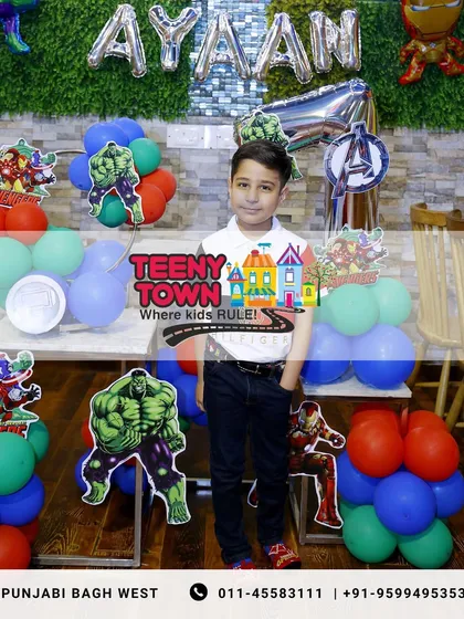 The birthday boy posing proudly in front of his Avengers-themed party setup.