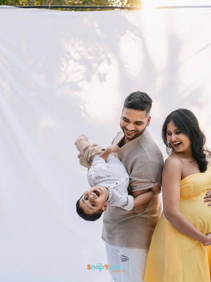 Using a simple white backdrop outdoors creates a unique studio-in-nature feel. This playful shot captures the family's laughter and excitement for their new addition.