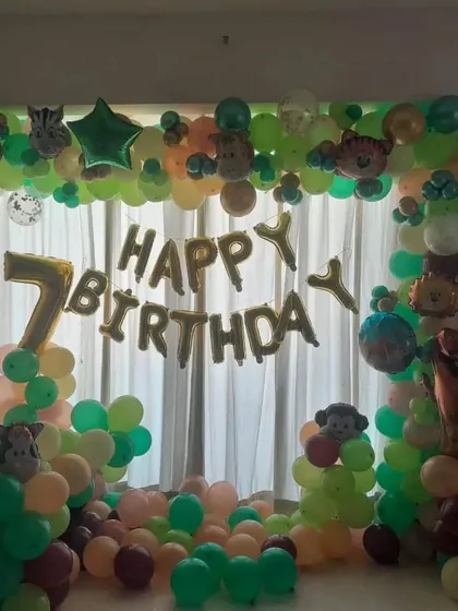 A jungle-themed 7th birthday party. This home decoration includes a "Happy Birthday" foil balloon banner and a balloon arch with animal accents.