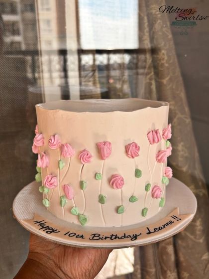 This delicate cake features hand-piped pink tulips on a pale pink whipped cream base. It's a simple, minimalist design that is both elegant and sweet.