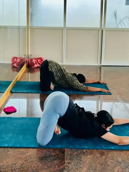 Two students in a synchronized stretch, reflecting in the studio mirror. This shows the focus and shared rhythm we cultivate in our classes.