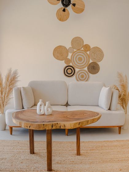This simple yet elegant seating arrangement features a comfortable sofa flanked by pampas grass in ceramic vases. The wall is adorned with a collection of woven plates, adding a touch of boho charm and textural interest.