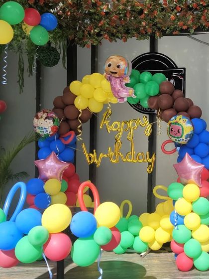A colorful outdoor Cocomelon-themed birthday decoration. The balloon arch uses bright primary colors to match the cartoon's theme.