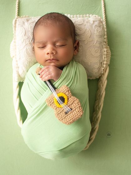 A tiny musician. This newborn is swaddled in a green wrap and holding a miniature crocheted guitar.