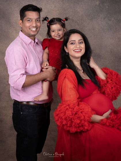 A happy family portrait featuring an expecting couple and their young daughter, all smiling for the camera during their maternity session.