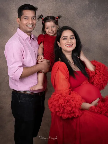 A happy family portrait featuring an expecting couple and their young daughter, all smiling for the camera during their maternity session.