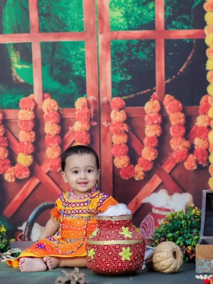 A happy baby girl dressed as Radha for Janmashtami, with a sweet smile and a pot full of cotton 'butter'. A beautiful way to celebrate the festival.
