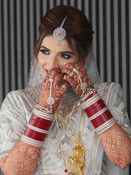 A playful and shy moment from the bride. This image showcases her beautiful henna, her traditional red chooda, and her radiant smile.