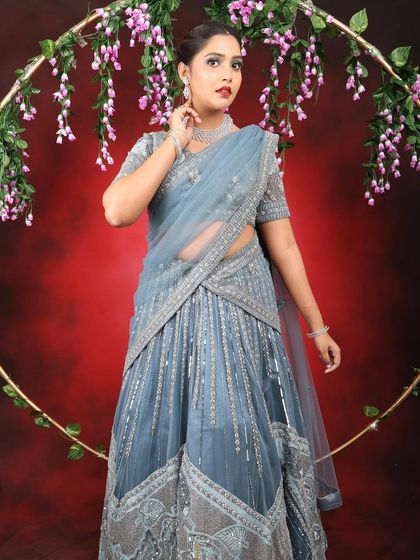 The full look against a floral ring backdrop. The makeup is balanced and elegant, designed to complement the heavily embellished grey lehenga without being overpowering.