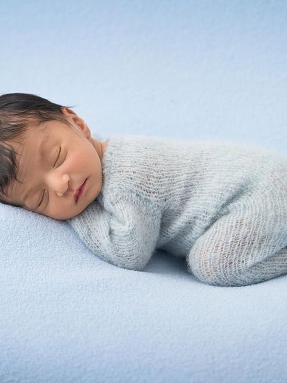 The perfect sleepy pose. A newborn in a soft blue sleeper is curled up on a simple, matching blue blanket, showcasing their peaceful slumber.