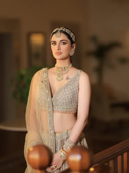 A front-facing portrait of the bride. The styling is clean and elegant, allowing the intricate details of the golden lehenga and jewelry to shine.
