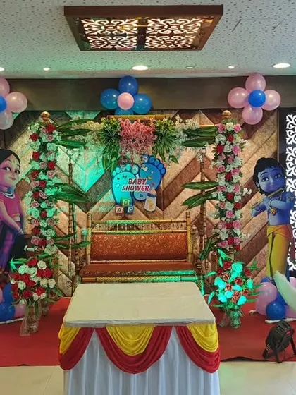 A symmetrical and elegant baby shower stage design. It includes a central jhula, a crescent moon prop, and character cutouts, all framed by beautiful floral arrangements and balanced lighting.