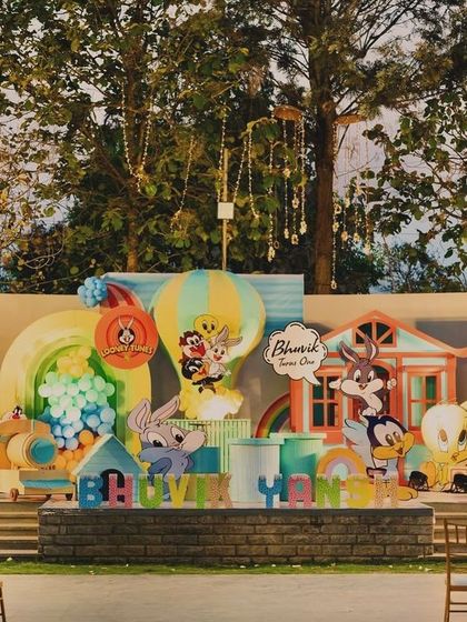 A grand and colorful Looney Tunes first birthday stage for Bhuvik. This massive outdoor setup features all the iconic characters, from Bugs Bunny to the Tasmanian Devil, in a playful and dynamic scene.