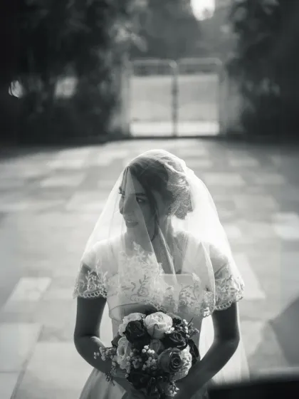 A moody and atmospheric black and white portrait of a bride holding her bouquet. The soft focus and composition give this image a timeless, vintage feel.