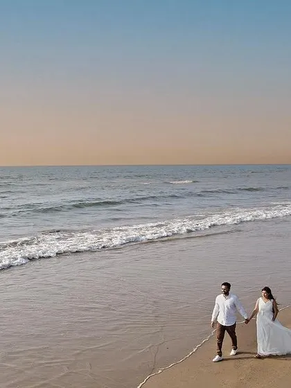 A wide aerial shot of a couple walking hand-in-hand along a deserted beach at sunset. Drone photography allows me to capture the vastness of the landscape and the intimacy of the moment simultaneously.