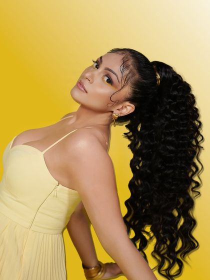 A profile view of the model with the high curly ponytail, highlighting the volume and texture of the hairstyle.