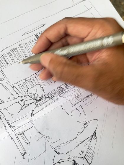 A close-up of my hand as I work on the pen sketch of the bookstall, adding details to the figures and shelves.