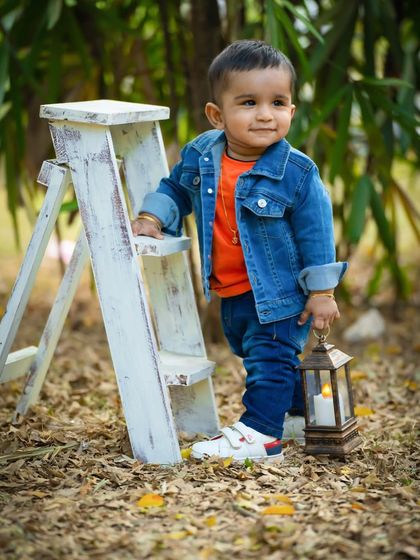A stylish little dude in his denim jacket, posing by a ladder prop in a beautiful park. Outdoor sessions are great for capturing active toddlers.