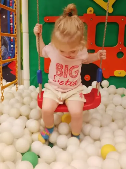 A "Big Sister" enjoys a gentle swing over the ball pit in our dedicated toddler area.