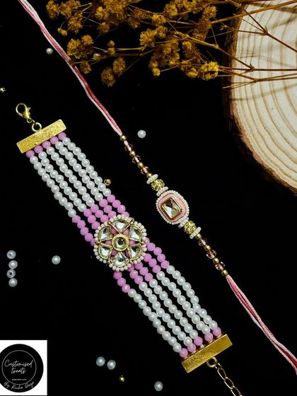 A stunning multi-strand pearl Lumba rakhi paired with a delicate single-strand rakhi. The pink and white beadwork offers a sophisticated and graceful look.