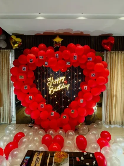 A heartfelt birthday surprise featuring a large heart-shaped balloon frame, perfect for clipping on memorable photos. The setup is completed with a neon sign and balloons covering the floor.
